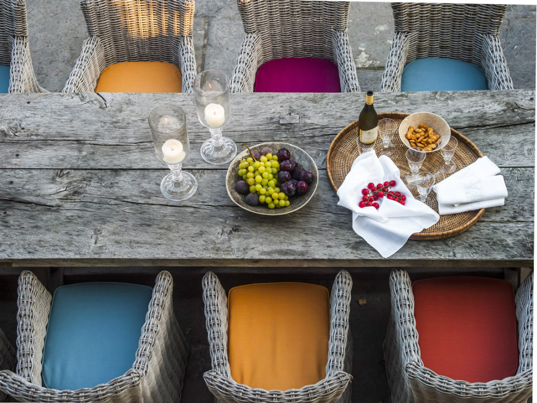 Colorful upholstered cushions and weathered dining table at The Little Monastery, a wonderful B&B near Bruges. Come enjoy photos and a tour of Belgian Design Style Inspiration from antiques dealers Alain and Brigitte Garnier.