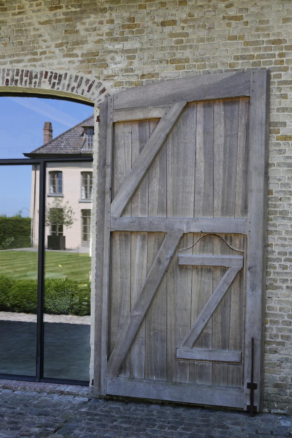 Rustic planked door, old brick, and historic buildings at The Little Monastery, a wonderful B&B near Bruges. Come enjoy photos and a tour of Belgian Design Style Inspiration from antiques dealers Alain and Brigitte Garnier.