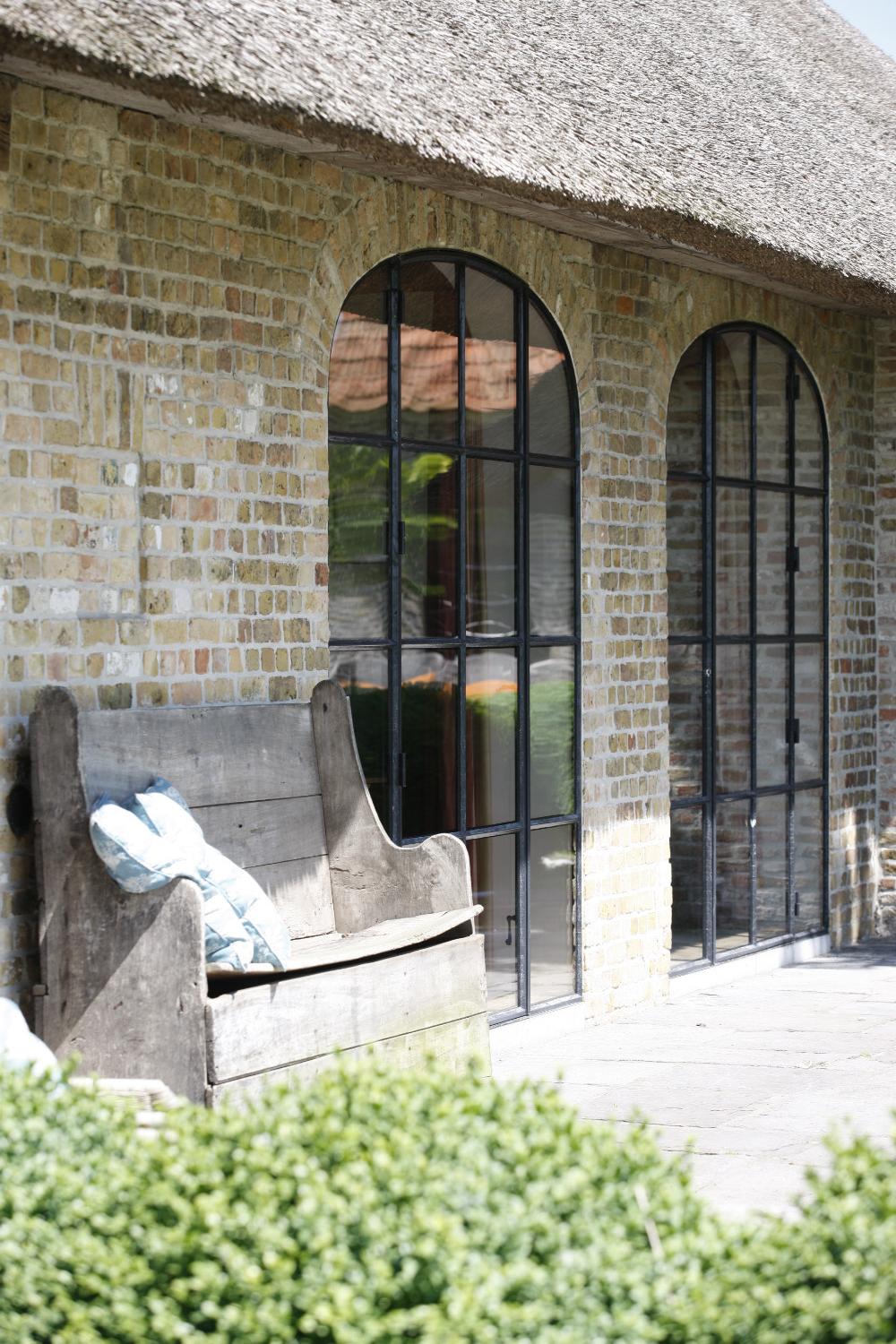 Arched steel and glass doors, old brick, and an ancient wood bench at The Little Monastery, a wonderful B&B near Bruges. Come enjoy photos and a tour of Belgian Design Style Inspiration from antiques dealers Alain and Brigitte Garnier.